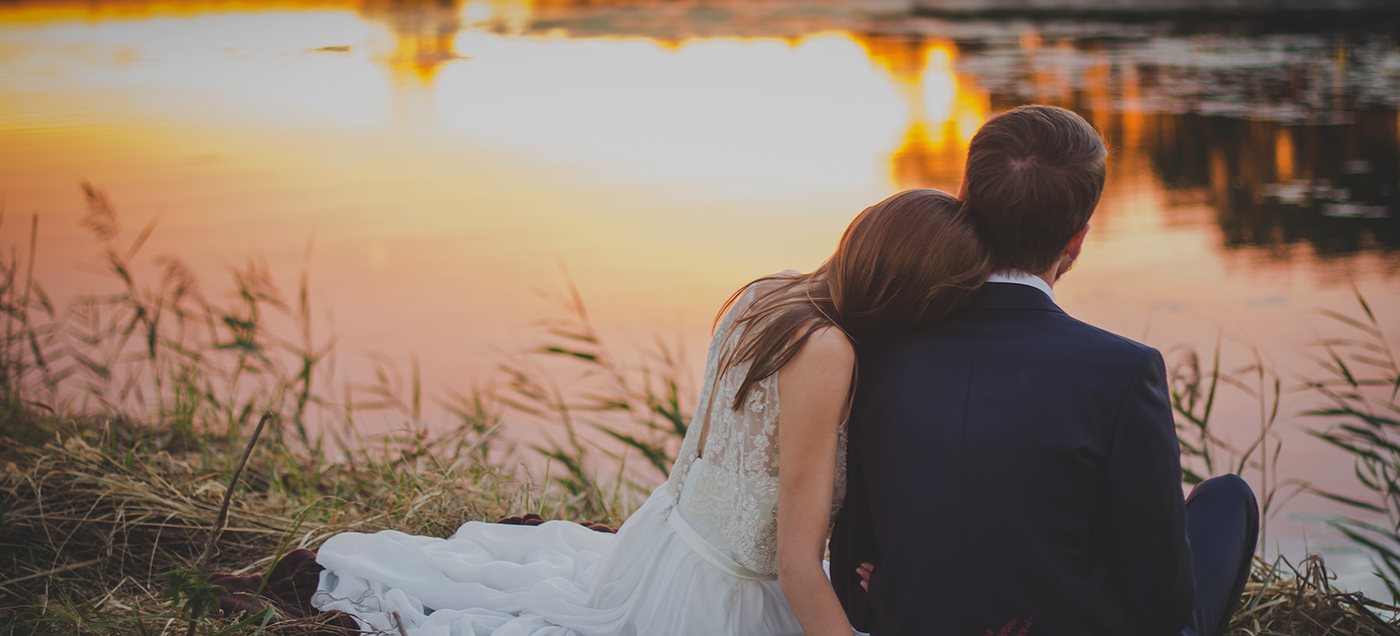 A couple sitting together by the water at sunset